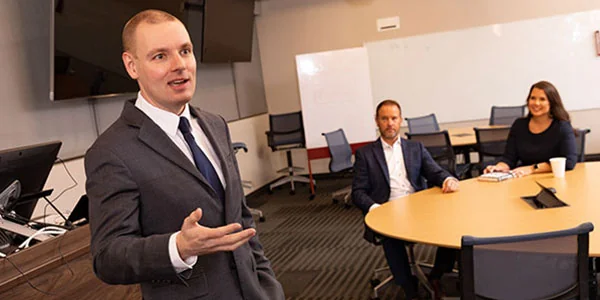 A young professor wearing a suit speaking to a class of students